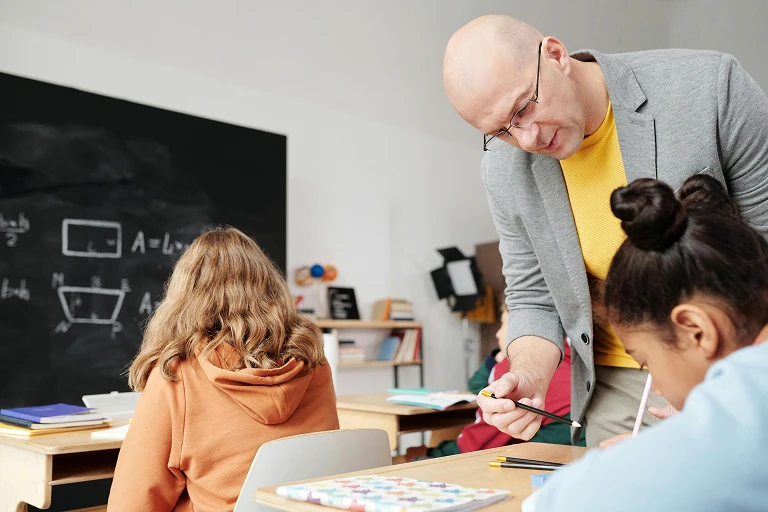 Adult helping a child with reading or writing at a table in a school setting