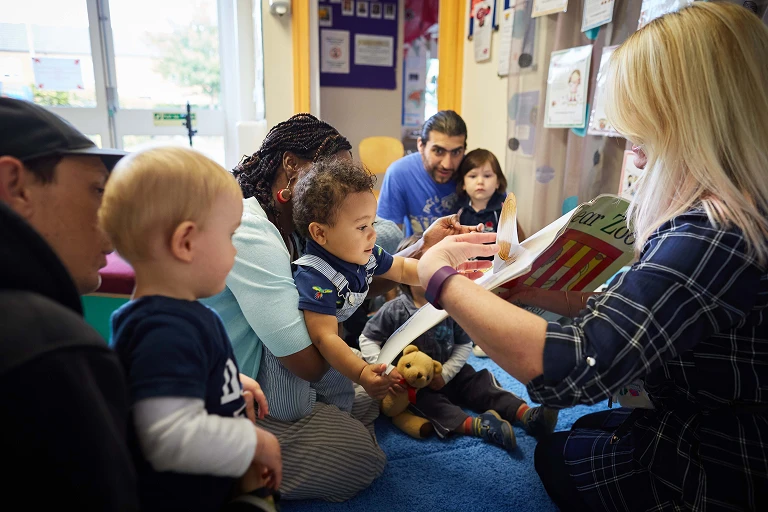 Adult reading a book aloud to a group of babies and young children
