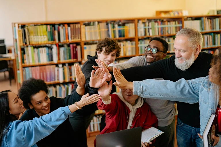 Group of adults and young people gathered in a library and raising their hands