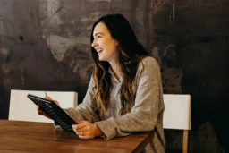 Adult smiling while seated at a table and holding a tablet