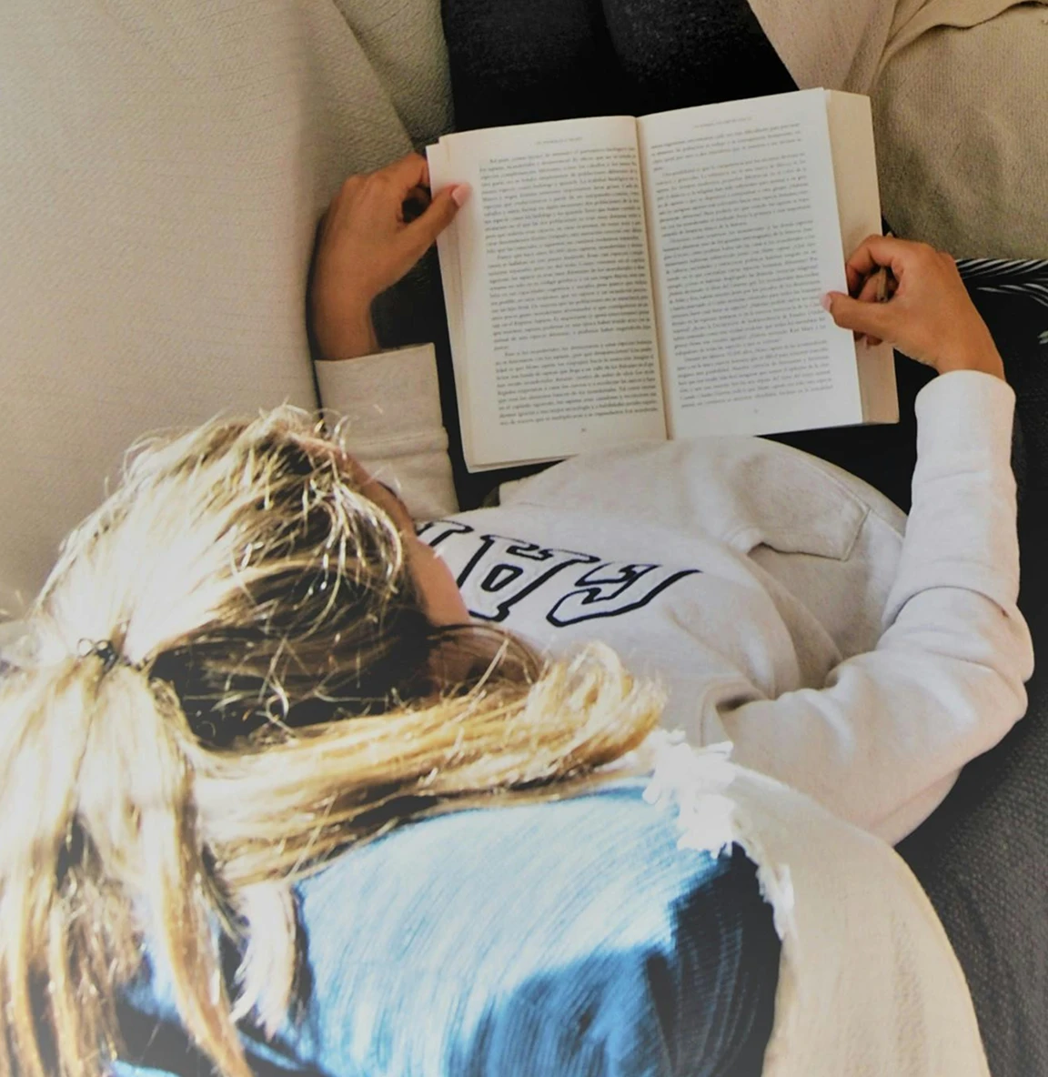 Lady lying on a sofa reading a book wearing a sweatshirt