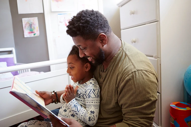 Adult and child reading a book together at a table