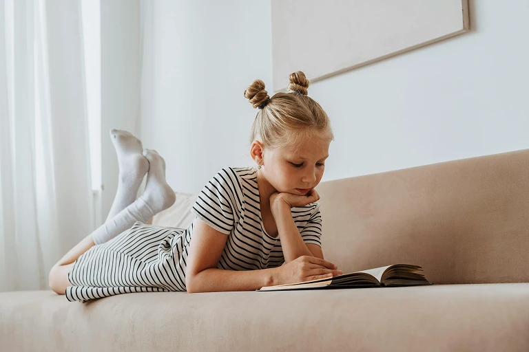 Child lying on a sofa and reading a book