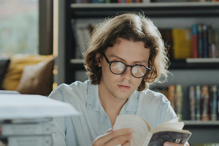 Young adult reading a book at a desk indoors