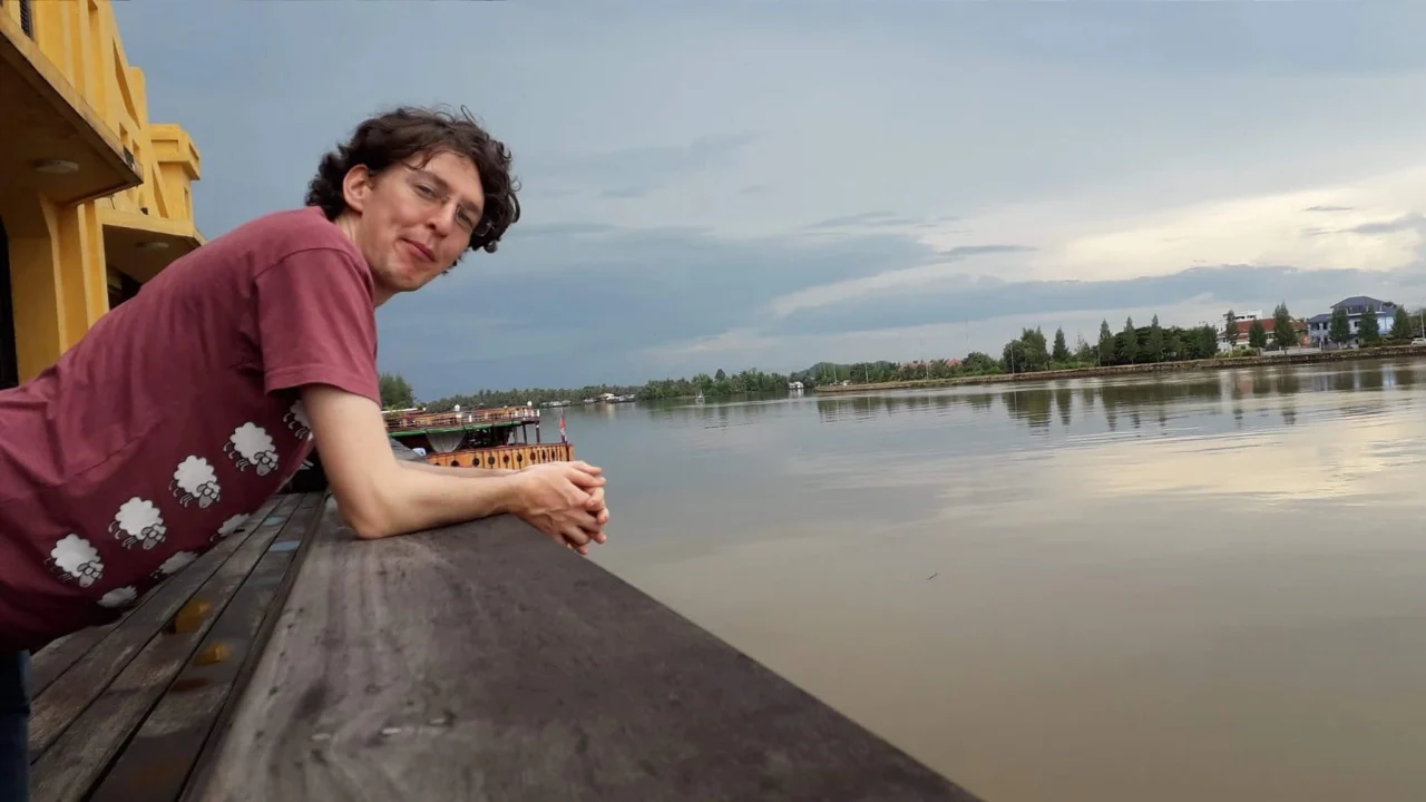 Adult sitting outdoors near water and reading a book