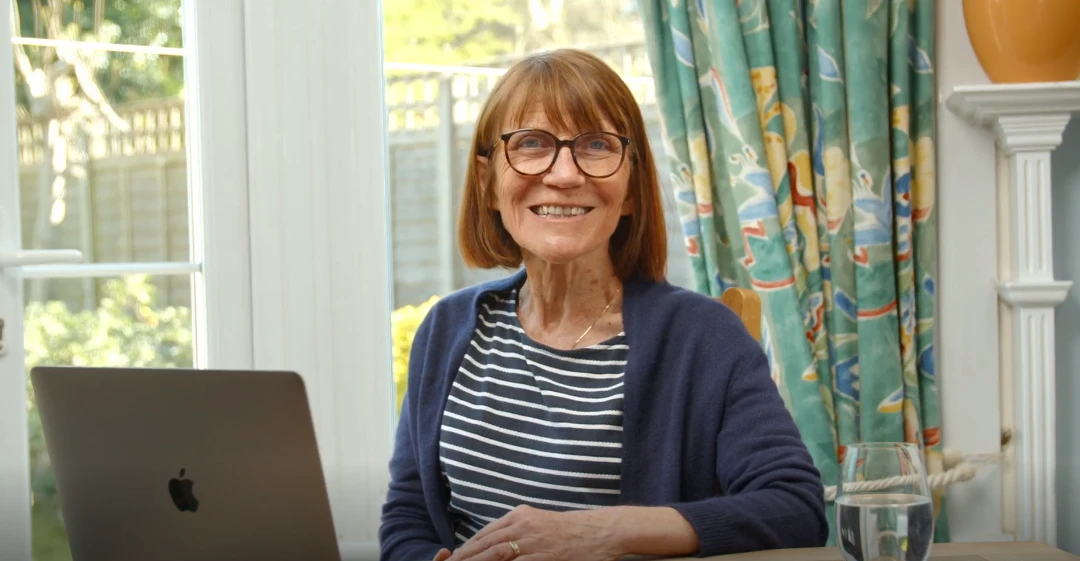Adult smiling while seated indoors, holding a book or papers