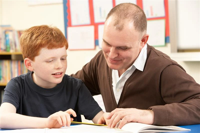 Adult supporting a child while reading a book together at a table