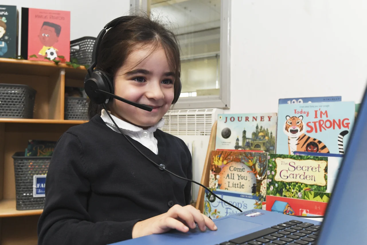 Young child wearing a headset and using a laptop in a classroom setting