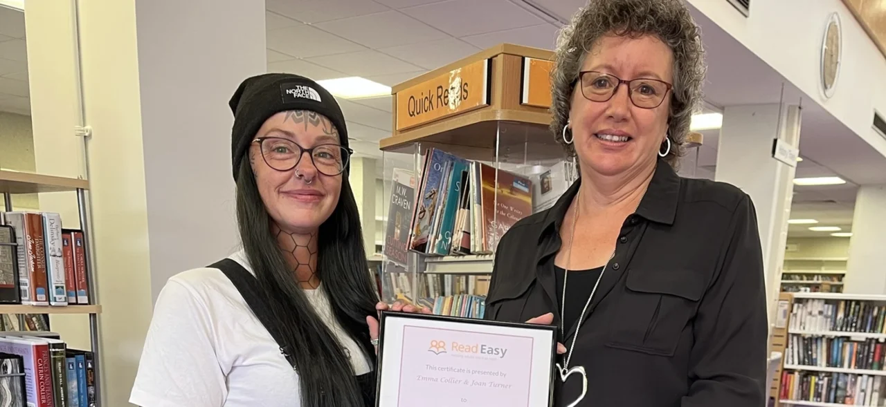 Two adults standing in a library holding a certificate