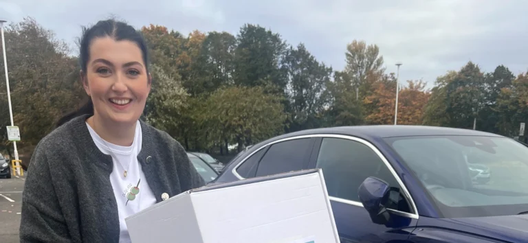 Adult standing beside a car holding a box of donated books