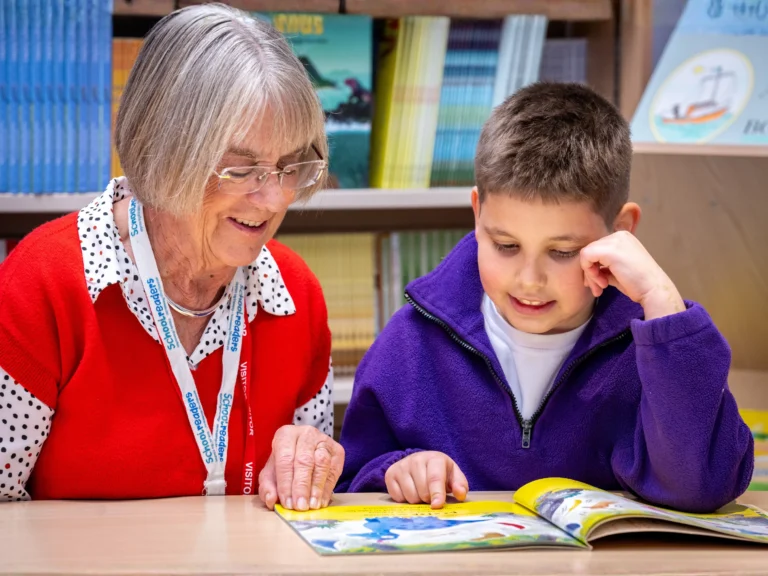 Adult supporting a child while reading a book together at a table