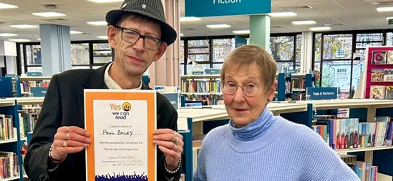 Two adults in a library holding a reading-related certificate