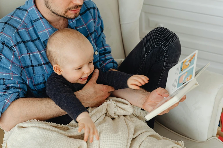 Adult holding a baby while sharing a book together at home