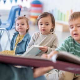 Young children sitting together in a classroom setting, reading books with adult support