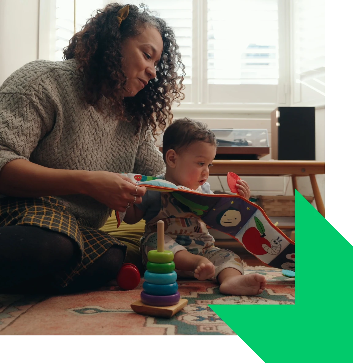 A early years practitioner sitting on the floor with a young baby looking at a sensory picture book