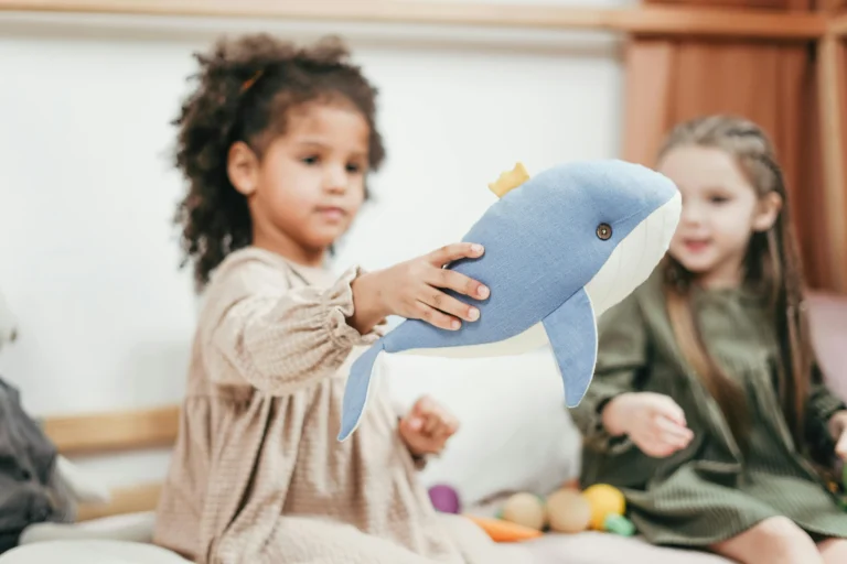 Young child holding a soft toy while looking at a book during playtime