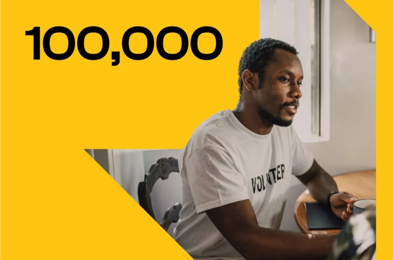 Adult volunteer sitting at a table and reading with a child in a learning setting next to the figure one hundred thousand