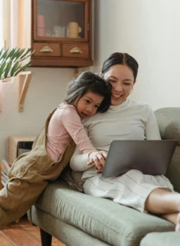 Woman and a young girl sitting on a sofa hugging and reading on a tablet together