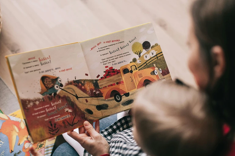 A female caregiver reading a picture book to a young child