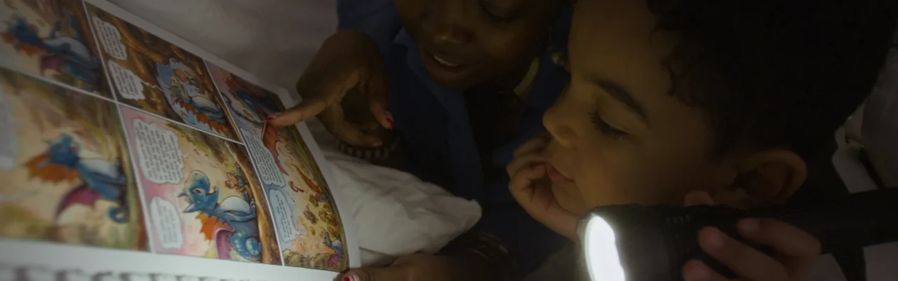 Two young boys reading comics under the bedsheets with a torch