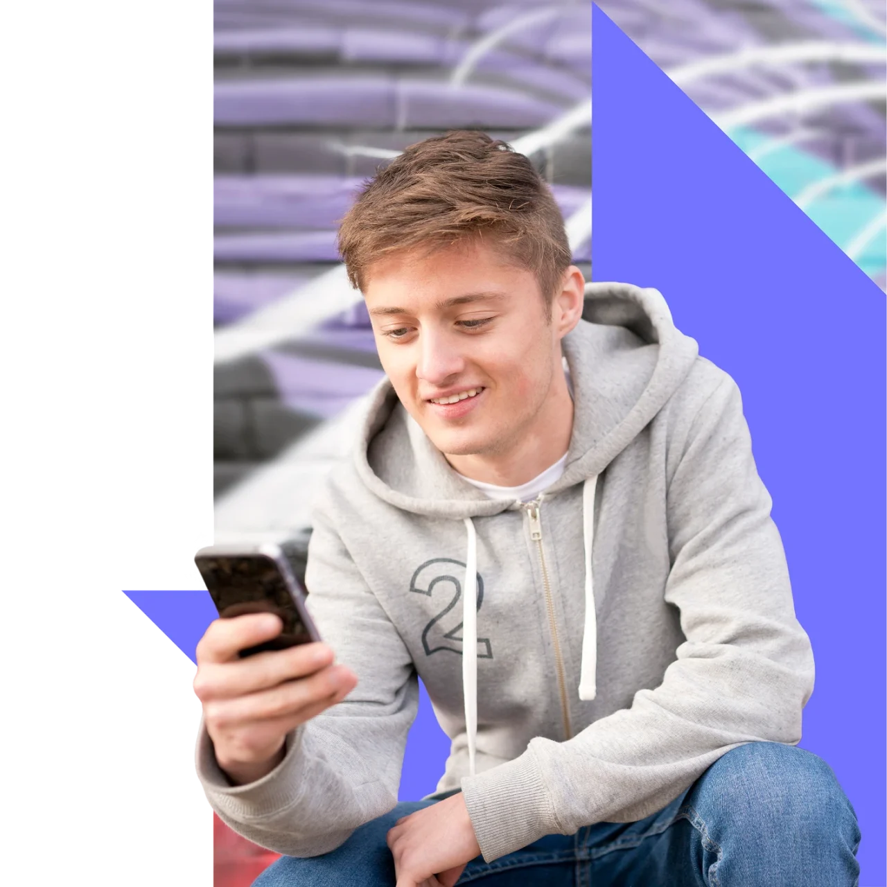 Teen boy crouching in front of graffiti wall using his phone