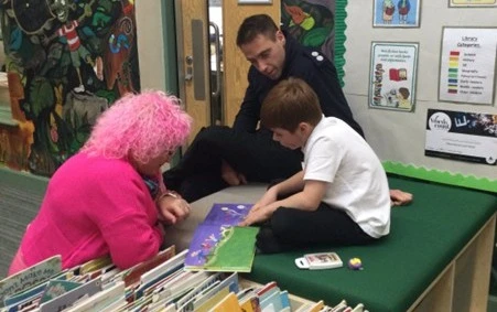 A man in firefighter uniform and a woman looking at a book with a primary school aged child in school