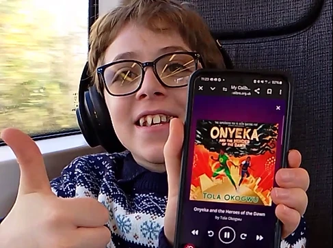 A boy holding up a phone showing the cover of an audio book