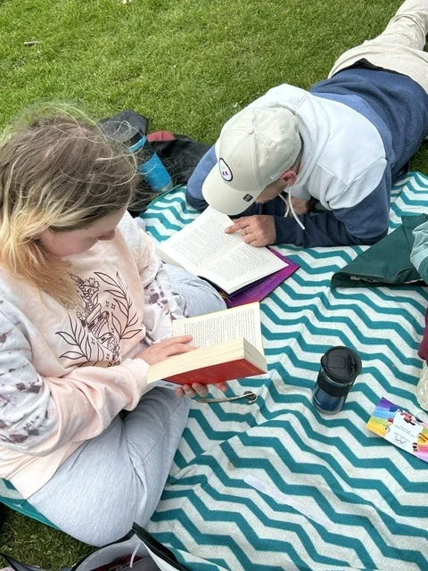 Two people reading outside on a picnic blanket